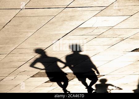 Silhouette ombra sfocata di giovani che camminano, ragazza con le mani sui fianchi e un ragazzo su una bicicletta dietro di loro Foto Stock