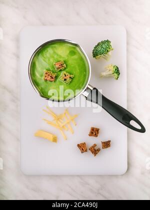 Zuppa di broccoli con crostini in pentola su tagliere bianco. Scatto in testa. Ricetta Foto Stock