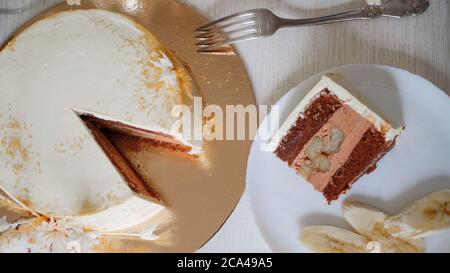 Bella torta di nozze cioccolato con crema di cioccolato all'interno e banana ripieno, pezzo di torta su un piatto. Torta bianca con decorazioni in cotone. Foto Stock