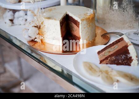 Bella torta di nozze cioccolato con crema di cioccolato all'interno e banana ripieno, pezzo di torta su un piatto. Torta bianca con un decor. Foto Stock