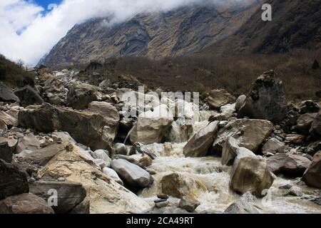 Fiume di montagna e cascata che scorre attraverso le rocce nella valle del Massiccio di Annapurna sul trekking ABC del Nepal Foto Stock