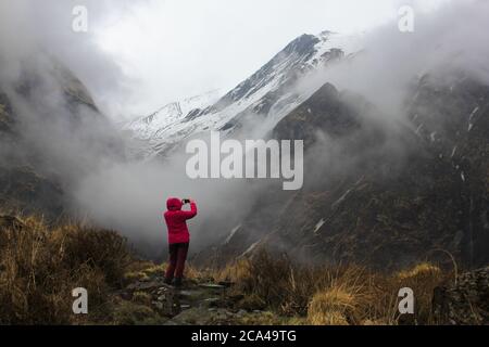 Machapuchare / Nepal - Novembre 2019: Trekker in un luminoso sta scattando una foto di Machapuchare nuvoloso e foggy pick in montagna Himalayan sul trek ABC Foto Stock