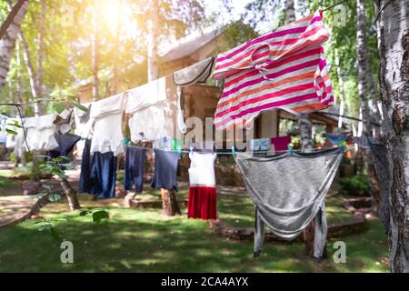 Scena di vita reale domestica di molti bambini e adulti vestiti puliti lavati appesi su stendibiancheria di betulla con spille. Cortile di casa su luminoso sole Foto Stock