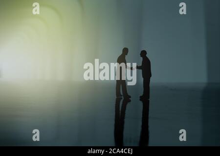 Silhouette di due uomini d'affari fare un accordo di partenariato stretta di mano. Fotografia concettuale di figure di persone in miniatura Foto Stock