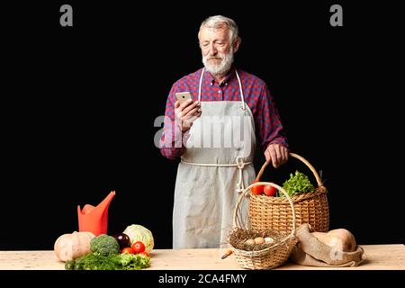 L'uomo anziano del villaggio che sta testando il messaggio a sua moglie su smartphone, guardando ansioso circa il suo essere in ritardo, andando cucinare la cena per due, comprata in fa biologica Foto Stock