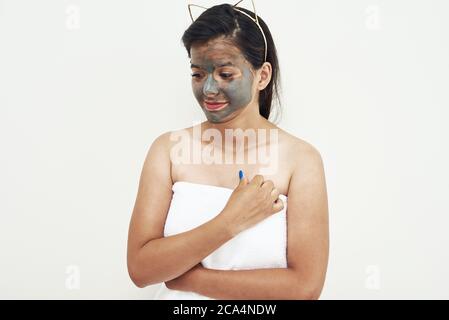 Trattamenti di bellezza Spa, cura della pelle. Giovane donna che applica facciale grigio fango argilla maschera al suo viso. Foto Stock