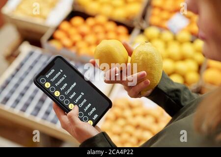 Primo piano di donna che usa la lista di controllo sullo smartphone nel supermercato mentre acquista i limoni Foto Stock