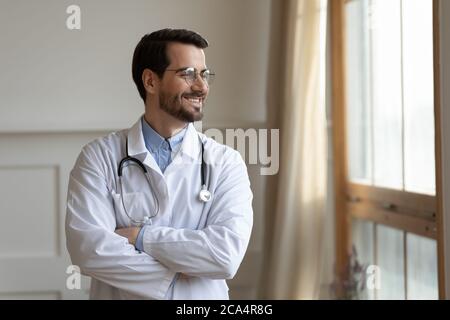 Sorridente giovane medico che pianifica la carriera futura, in piedi vicino alla finestra. Foto Stock