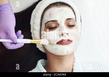 Concetto di spa. Giovane donna con maschera nutriente viso in salone di bellezza, primo piano. L'estetista applica una maschera idratante al viso del cliente. Foto Stock