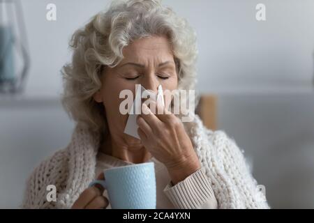 Donna anziana malsana che soffia naso che cola bevande antivirali Foto Stock