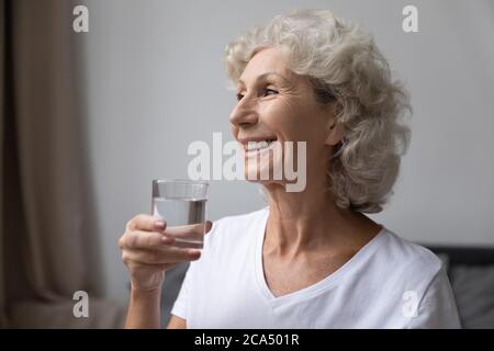 Donna anziana sorridente che tiene un bicchiere di acqua ferma Foto Stock