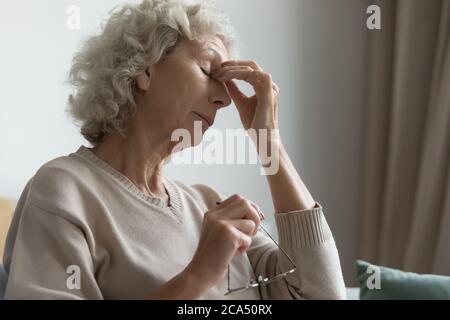 La donna anziana ha tolto gli occhiali per alleviare i sentimenti degli occhi Foto Stock