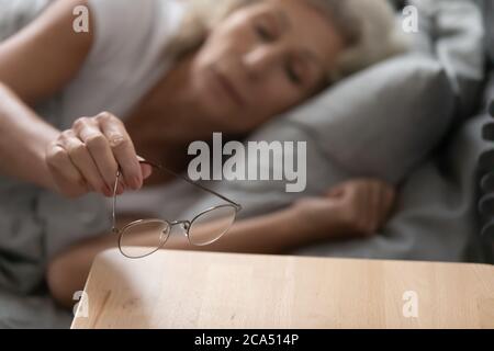 La donna anziana ha tolto gli occhiali li ha messi sul closeup del comodino Foto Stock