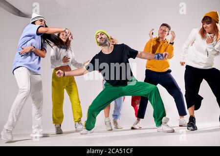 Esecuzione di bel ballerino maschile break, in piedi con gambe larghe di fronte a gente allegra danza, mostrando hip hop film, focalizzato su proces Foto Stock