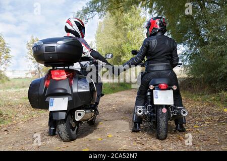 Due motociclisti che tengono le mani mentre si siedono sulle motociclette Foto Stock