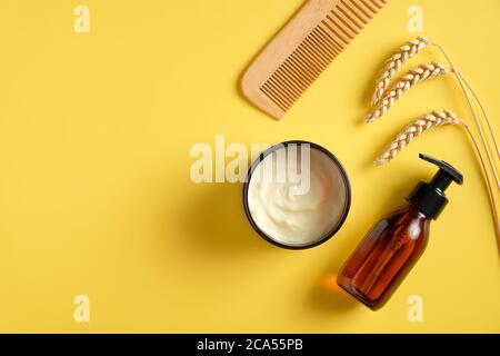 Cosmetici naturali SPA su sfondo giallo. Flacone a pompa piatto in vetro ambrato con gel doccia, crema idratante per il corpo, pettine per capelli. Bagno beau Foto Stock