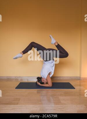 donna anonima che inizia sostenuto posizione del supporto per il capo. Vista laterale di una donna slim che fa yoga in un accogliente soggiorno durante il giorno a casa. Foto Stock