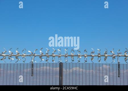 Area riservata. Primo piano di recinzione di sicurezza con filo spinato contro un cielo blu Foto Stock