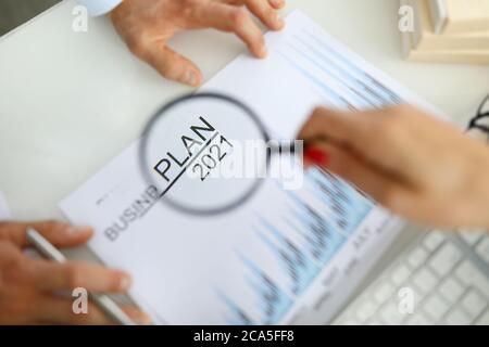 La mano della donna tiene la lente di ingrandimento sopra il programma di affari per 2021 Foto Stock