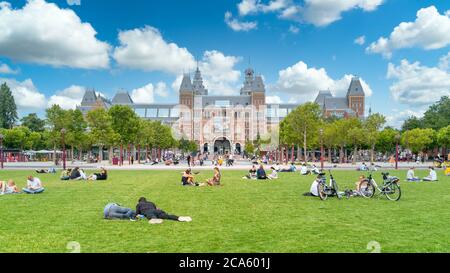 Amsterdam, Paesi Bassi - 23 luglio 2020 - turisti seduti sull'erba della piazza del museo di fronte al Rijksmuseum (museo federale) nel c Foto Stock