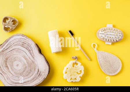 Incorniciate da spugne di loofah, massaggiatore, spazzolino da denti, pettine di legno, fetta di legno sulla superficie gialla. Raccolta per bagno da materiale ecologico. Zero sprechi Foto Stock