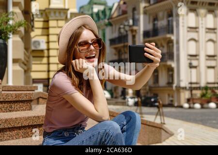 Bella giovane donna turista seduto sulle scale utilizzando smartphone facendo videochiamata o selfie Foto Stock