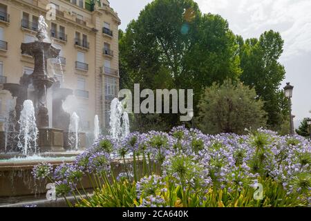 Fontana di battaglie a Granada circondata da fiori viola di agapanto (Agapanthus africanus) bagnati da acqua rinfrescante Foto Stock