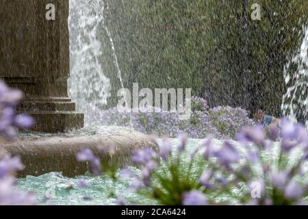 Fontana di battaglie a Granada circondata da fiori viola di agapanto (Agapanthus africanus) bagnati da acqua rinfrescante Foto Stock