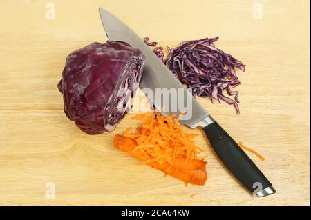 Ingredienti di coleslaw, cavolo rosso e carota con un coltello su una taglierina di legno Foto Stock