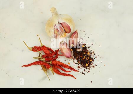 Bulbo d'aglio e chiodo di garofano con peperoncino secco e fiocchi su una superficie di lavoro in marmo Foto Stock