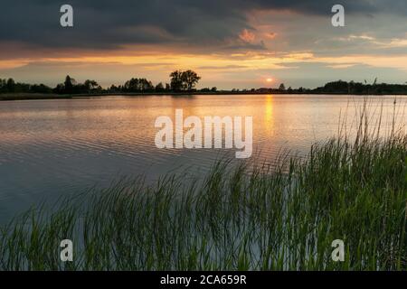 Tramonto e nuvole scure su un lago tranquillo con canne verdi Foto Stock