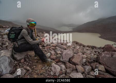 Un'escursione biologa attraverso la Cordillera Vilcanota fa una pausa e si siede su una pietra alta nelle Ande montagne dove c'è poco ossigeno. Foto Stock