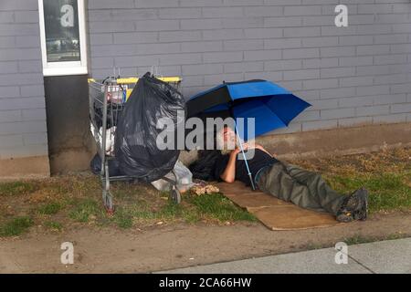 Senzatetto uomo che dorme sotto un ombrello accanto a una strada a Vancouver, BC, Canada Foto Stock