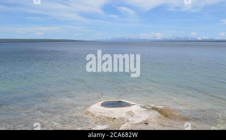 Primavera a Yellowstone: Geyser Big Cone nel bacino occidentale di Geyser Thumb sulla riva del lago Yellowstone con la catena di Absaroka oltre Foto Stock