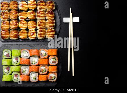 Set di sushi servito su un'ardesia di pietra su uno sfondo scuro. Panini di sushi con salmone, tonno, cetriolo, al forno, wasabi, salsa di soia e zenzero. Sushi Rolls phot Foto Stock