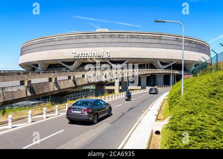 Le autovetture raggiungono l'edificio circolare del Terminal 1 dell'aeroporto di Parigi-Charles de Gaulle tramite la strada di accesso in una giornata di sole. Foto Stock