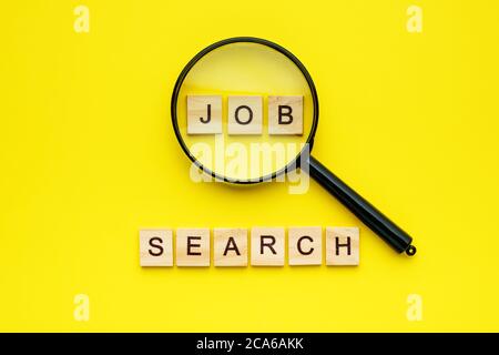 ricerca di lavoro con caratteri in legno e lente di ingrandimento su sfondo giallo. Foto Stock