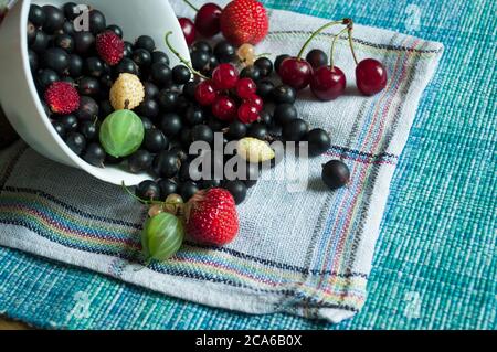 In un piatto bianco su sfondo blu, mescolare il ribes, le ciliegie, le fragole e i frutti di mare maturi e succosi. Berry sfondo, composizione con frutti di bosco Foto Stock