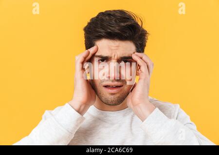 Foto di malato infelice uomo che ha mal di testa e che tocca i suoi templi isolati su sfondo giallo Foto Stock