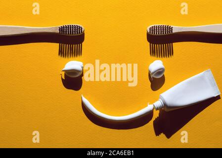 Spazzolini da denti e pasta di legno su sfondo giallo. Concetto dentale sotto forma di un volto divertente. Foto Stock