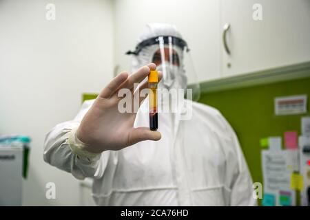 Vista ravvicinata di un medico o di uno scienziato medico in un laboratorio che indossa una tuta bio-protettiva, una maschera facciale, uno scudo facciale e guanti che assumono e mostrano un Foto Stock