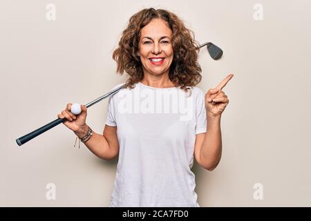 Media età bella sportivo che gioca a golf usando bastone e palla su sfondo bianco sorridente felice puntando con mano e dito a lato Foto Stock