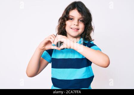 Carino bambino ispanico con capelli lunghi indossando abiti casual sorridente in amore facendo il simbolo del cuore forma con le mani. Concetto romantico. Foto Stock
