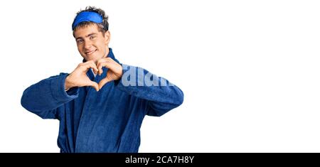 Giovane bell'uomo che indossa la maschera da sonno e l'accappatoio sorridente nell'amore mostrando il simbolo del cuore e la forma con le mani. Concetto romantico. Foto Stock