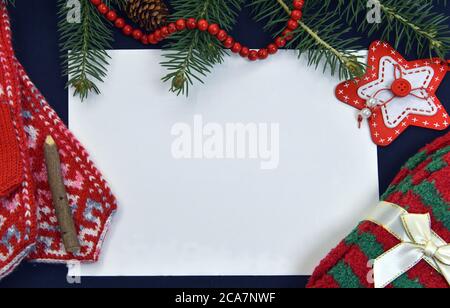 Carta vuota con mittens a maglia e calze su tavolo con conifera. Natale e Capodanno sfondo per carte, inviti, mockup. Vista dall'alto con COP Foto Stock