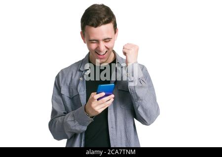 Un giovane in una camicia manatee, una t-shirt nera e pantaloni, isolati su bianco. sì, facendo un gesto di vittoria. Tenendo uno smartphone in mano Foto Stock