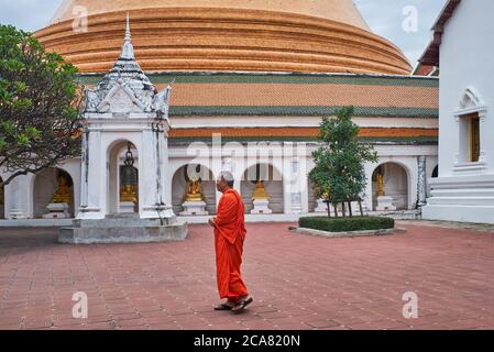 Un monaco cammina nei terreni di Phra Pathom Chedi, con un'altezza di 120 m il più alto chedi (stupa) in Thailandia (visto in b/g); situato in Nakhon Pathom Foto Stock