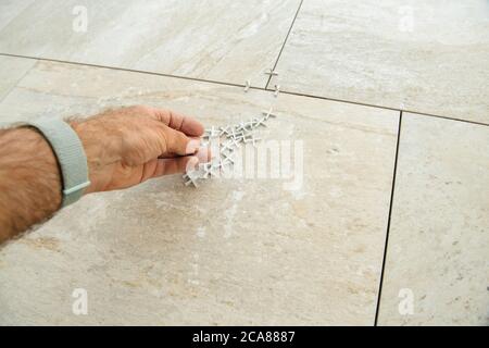 Installatore personale POV Perspective Worker che tiene più distanziatori per piastrelle durante l'installazione di nuove piastrelle di lusso sul pavimento Foto Stock