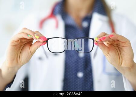 Donna in camice medico bianco tiene gli occhiali nelle sue mani. Foto Stock