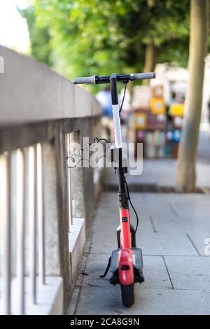 Scooter elettrico rosso parcheggiato e incatenato in modo sicuro a una recinzione. Eco-friendly verde moderno concetto di mobilità urbana di condivisione dei trasporti con l'elettricità Foto Stock